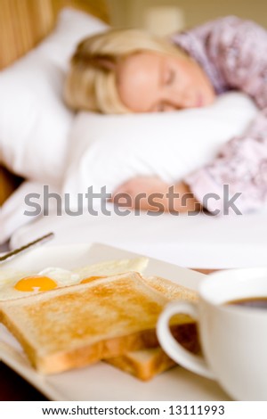 A young woman asleep in bed has breakfast waiting for her