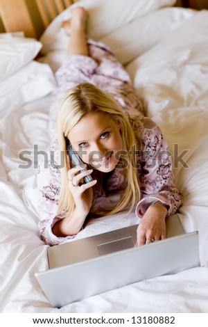 A young attractive woman using laptop computer and phone in bed