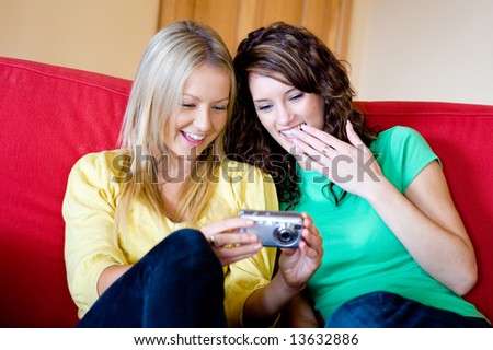 Two young women at home on the sofa with a digital camera