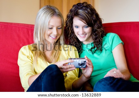 Two young women at home on the sofa with a digital camera
