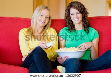 Two young women eating popcorn at home on the sofa
