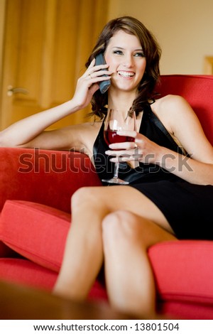A beautiful young woman in black dress sitting on sofa with phone and wine