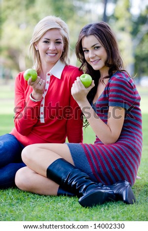 Two young attractive women sitting outside on the lawn with apples