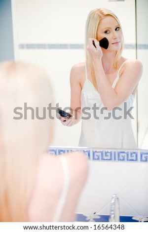 A young attractive woman in bathroom applying powder to her face