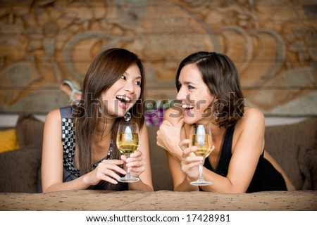 Two young attractive women with wine lying on bed
