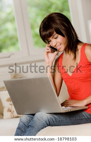 A woman sitting at home on the sofa with laptop computer and phone