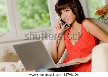A woman sitting at home on the sofa with laptop computer and phone