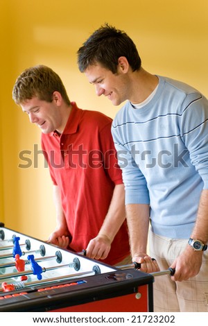 A young man playing table football indoors against a friend