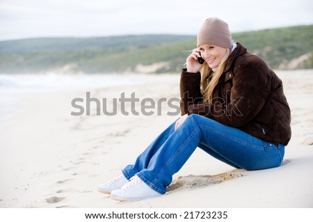 A young attractive woman outside on a beach in winter wear using mobile phone