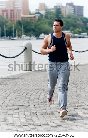 A good-looking man is out running by the side of a river in the city
