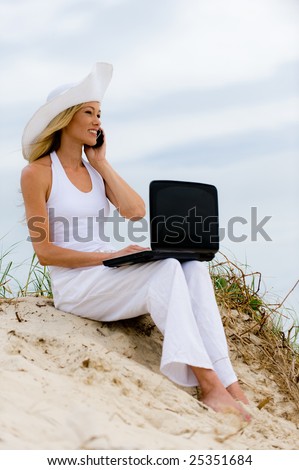 A young woman sitting on the beach with laptop computer and phone