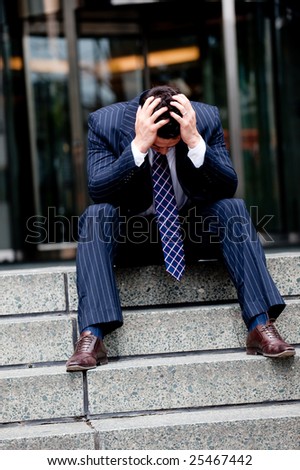 A distraught businessman sitting on steps with head in hands