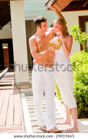 A young couple on vacation standing outside their villa with a coconut drink