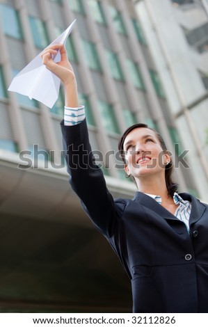 An attractive young businesswoman holding a paper plane against city backdrop