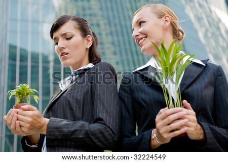 Two competitive businesswomen cupping their plants in their hands