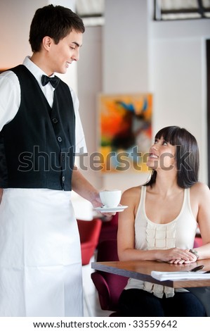 A young and attractive waiter serving coffee to a customer in an indoor restaurant