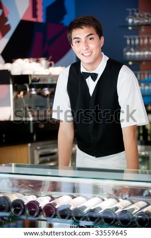 A young and attractive waiter stands behind the bar in an indoor restaurant
