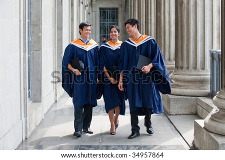 A group of graduates holding their mortar board in their hands and chatting along a hallway