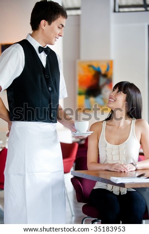 A young and attractive waiter serving coffee to a customer in an indoor restaurant