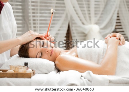Ear candling being carried out on an attractive caucasian woman in a spa