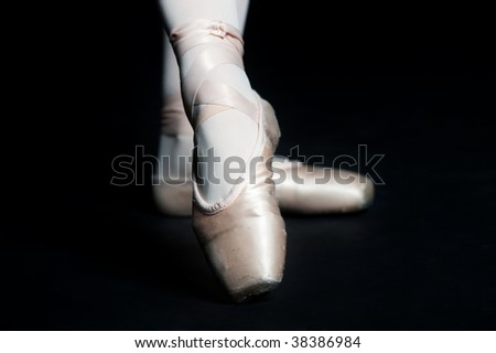 A pair of feet wearing ballet slippers posing on black background