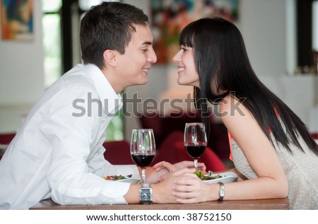 A young and attractive couple holding hands and about to kiss over their dinner in an indoor restaurant