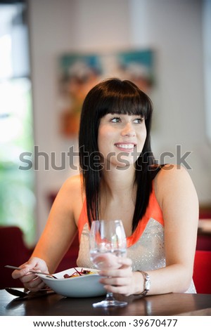 A young and attractive woman eating a salad in an indoor restaurant