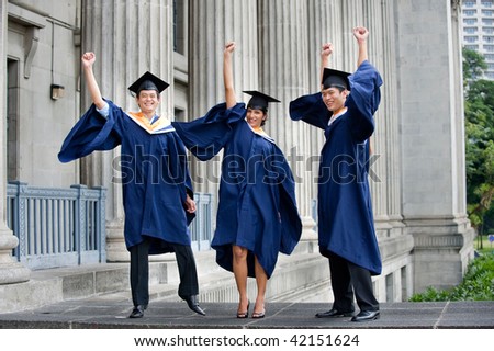 Three young graduates pump their fists in the air outdoors and celebrate their achievement
