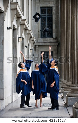 A group of graduates toss their mortar boards into the air in a hallway