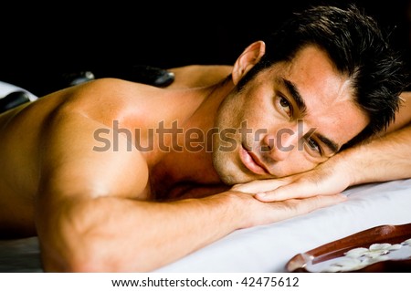 A good looking man lying on a massage bed with hot stones on his back