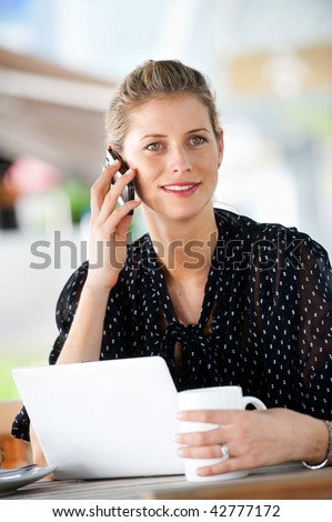 A young attractive caucasian woman using her phone and laptop outdoors at a cafeteria