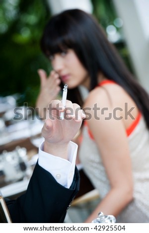 A young and attractive woman covers her nose to avoid the smoke from a cigarette at an outdoor dining area