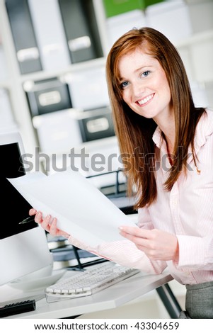 An attractive caucasian woman at her office desk with pen and paper in her hands