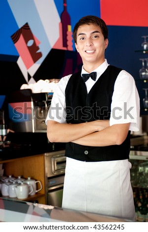 A young and attractive waiter stands behind the bar in an indoor restaurant