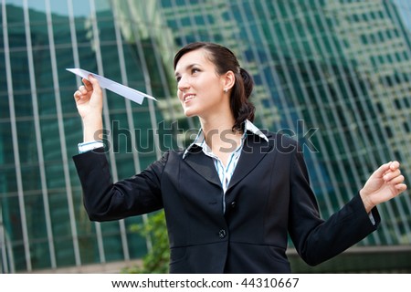 An attractive young businesswoman holding a paper plane against city backdrop