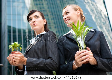 Two competitive businesswomen cupping their plants in their hands