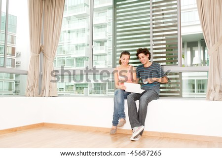 A young and attractive couple using laptop by the windows in their new home