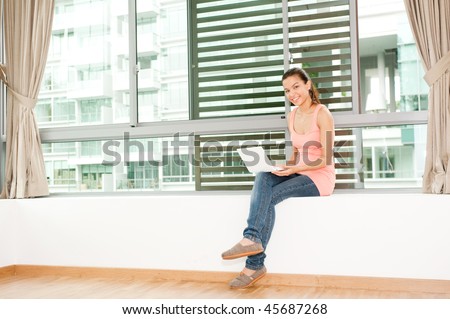 A young and attractive asian woman using her laptop by the windows in her new home