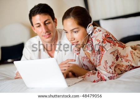 An attractive young couple lounging on their bed while making a video call on a laptop