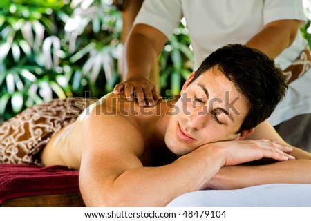 An attractive young man enjoying a back massage at a spa outdoors