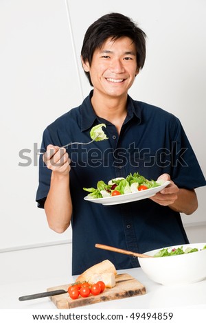 A good looking man eating a healthy meal of bread and salad in his kitchen
