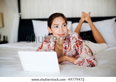 An attractive young woman lounging on her bed while making a video call on a laptop