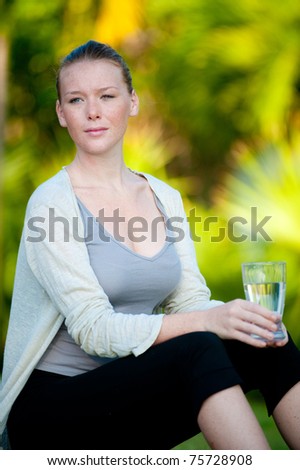 An attractive young woman sitting outside holding a glass of water