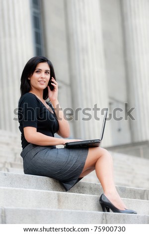 An attractive Indian businesswoman sitting outside with laptop and phone