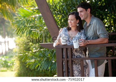 A young couple on vacation standing on the balcony holding mugs
