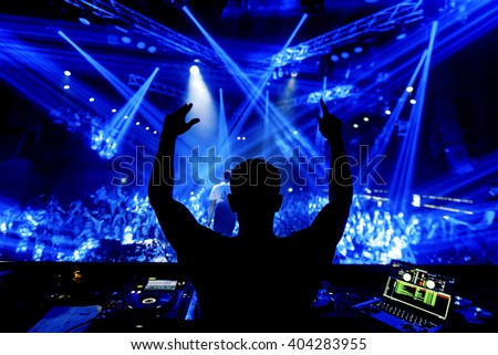 DJ hands up at night club party under blue light with crowd of people