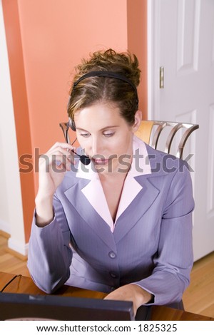 A young woman in business suit talking on a headset working from home