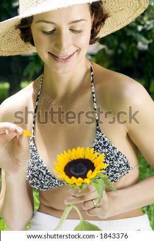 Attractive young woman with sunflowers wondering \'he loves me, he loves me not\' on a summers day in the park. Central Park, NY. USA.