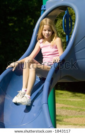 A young blonde girl plays on the slide at a local park.