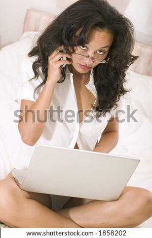 An attractive young asian woman works on her laptop whilst still in bed